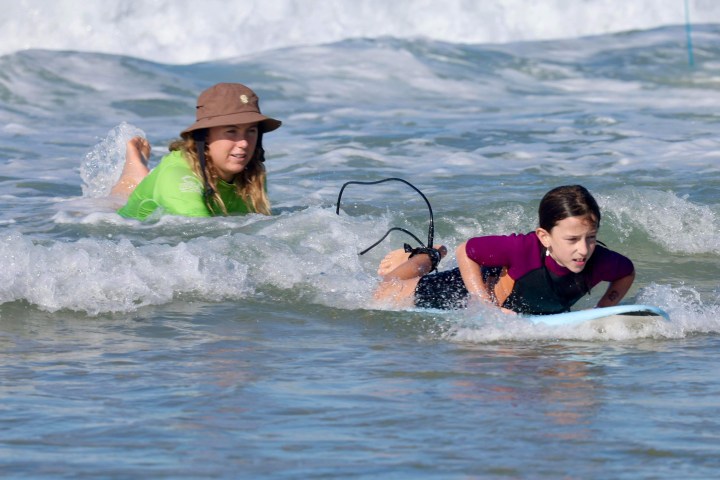 Two people lying on surfboards in the ocean, wearing wetsuits, with waves around them.
