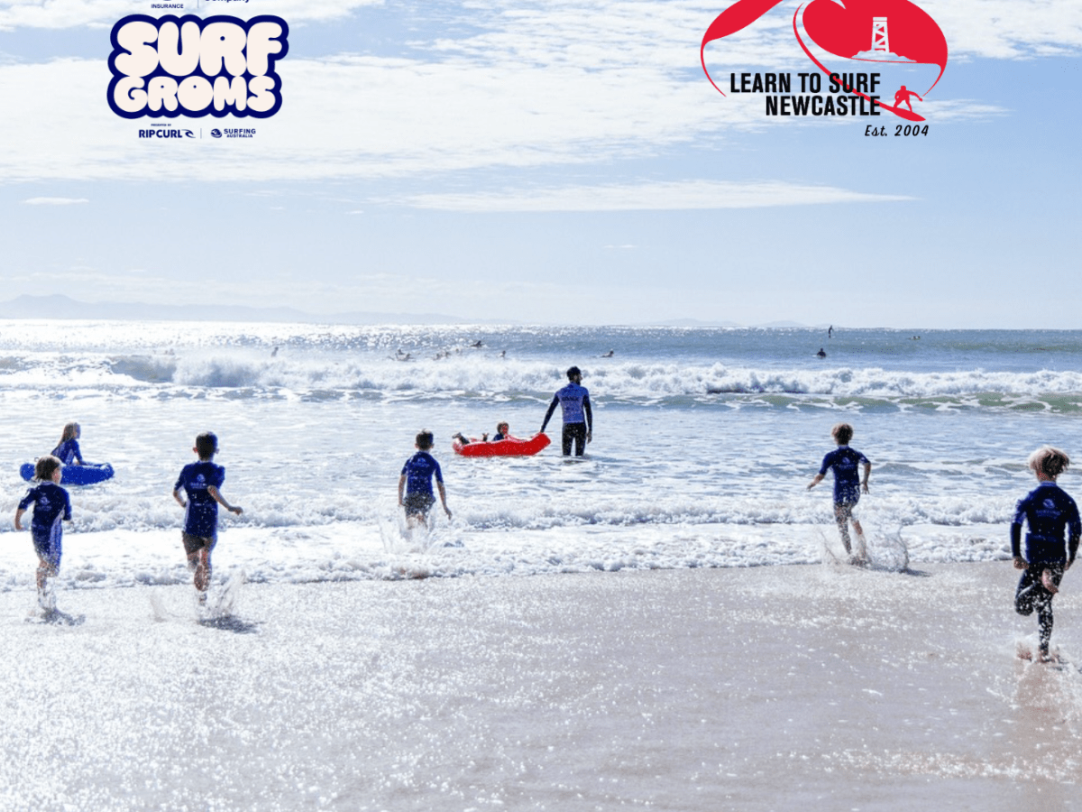 Group of surfers in blue shirts entering the ocean with surfboards on a sunny day.